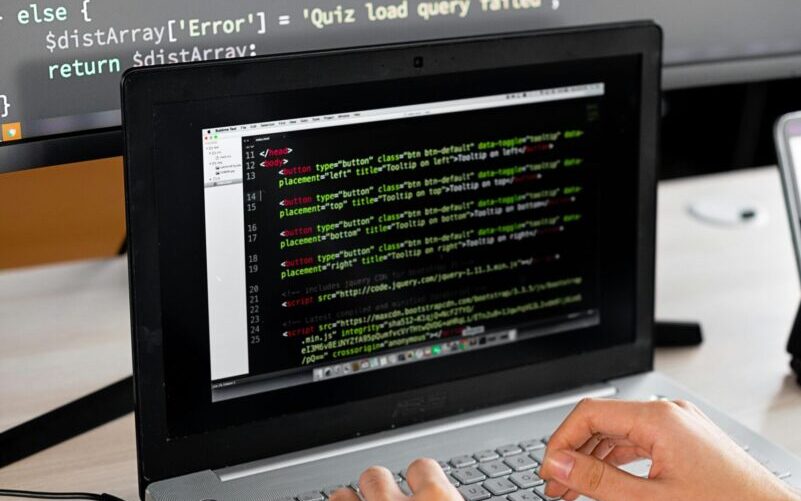 Person coding at a desk with laptop and external monitor showing programming code.