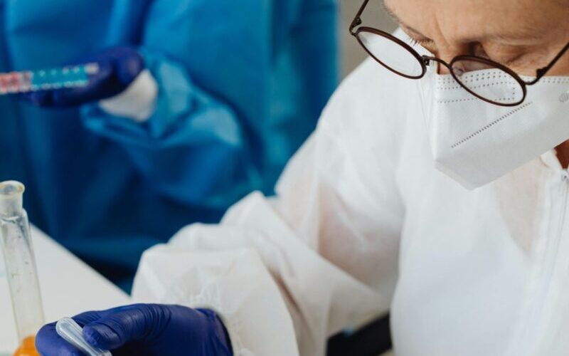 Scientist in protective gear using pipette with test tubes in a lab setting.